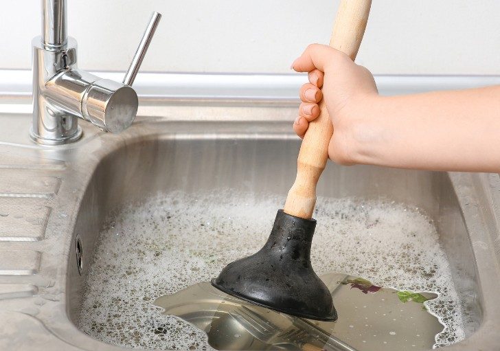 Ventosa en un fregadero con agua estancada Desatascador de ventosa con mango de madera en un fregadero lleno de agua estancada