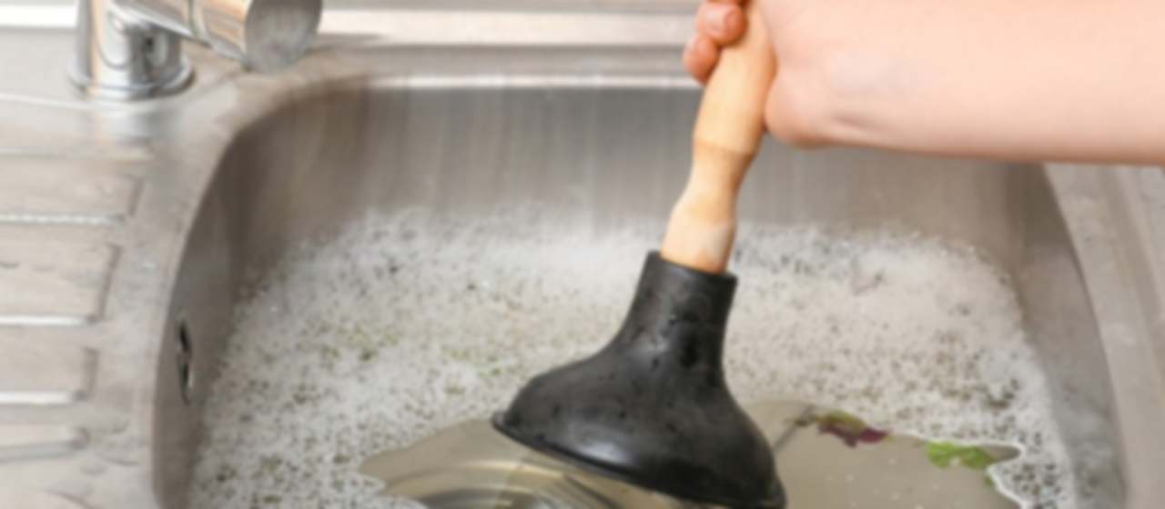 Desatascador de ventosa con mango de madera en un fregadero lleno de agua estancada