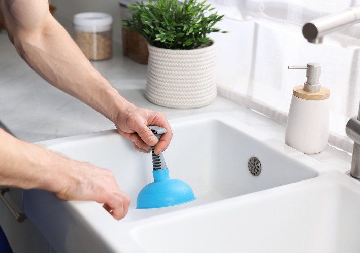Desatascador de ventosa en un lavabo Persona usando un desatascador de ventosa azul sobre el desagüe de un lavabo