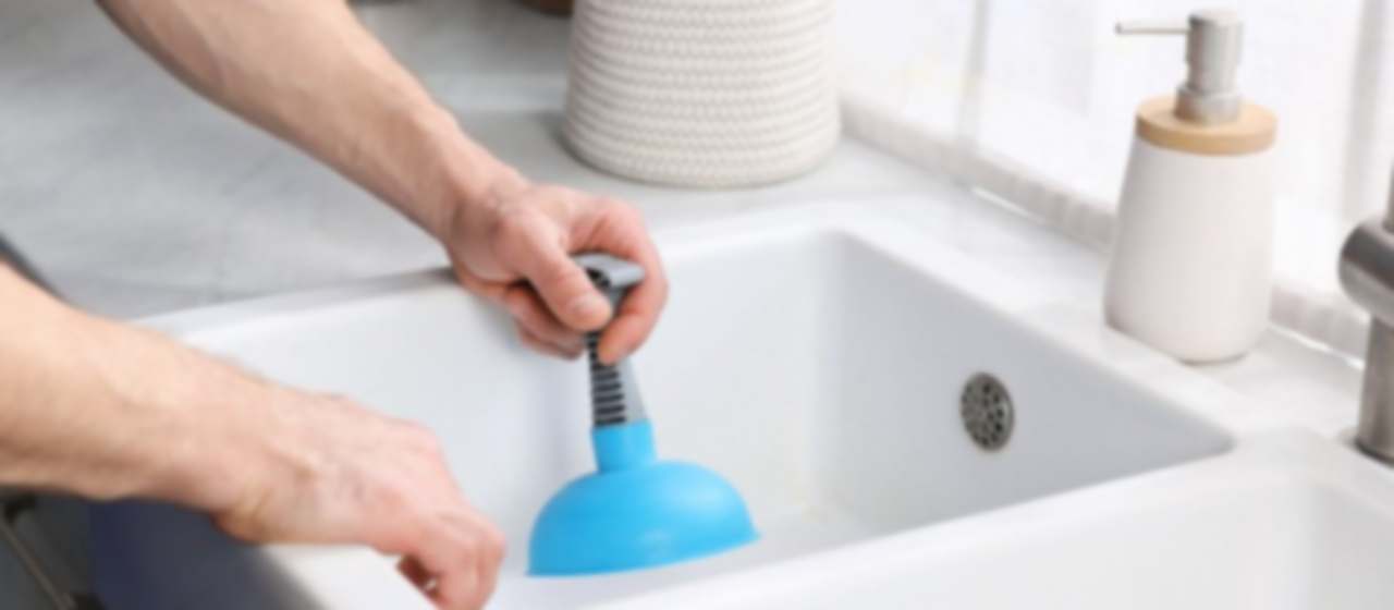 Persona usando un desatascador de ventosa azul sobre el desagüe de un lavabo