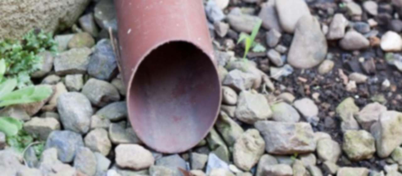 Tubo de bajante de pluviales desaguando sobre un lecho de grava en el jardín