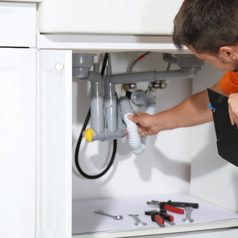Técnico revisando el sifón y el tubo de desagüe bajo el fregadero de una cocina