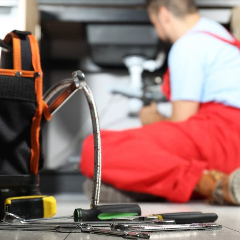 Técnico de desatascos trabajando bajo un fregadero con la bolsa de herramientas en primer plano