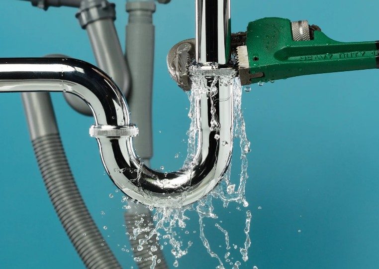 Fuga de agua en la unión de un sifón Agua saliendo a presión por la unión de un sifón cromado mientras se aprieta con una llave