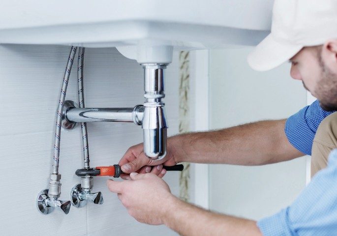 Revisión de llaves de escuadra bajo el lavabo Técnico ajustando con una llave las llaves de escuadra y el sifón cromado de un lavabo