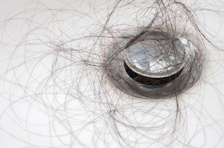 Pelos enredados alrededor de la rejilla del desagüe de un plato de ducha