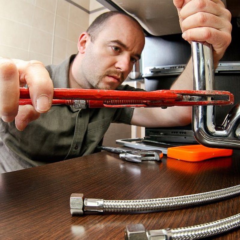 Técnico con llave grifa desmontando el sifón de un fregadero de cocina atascado