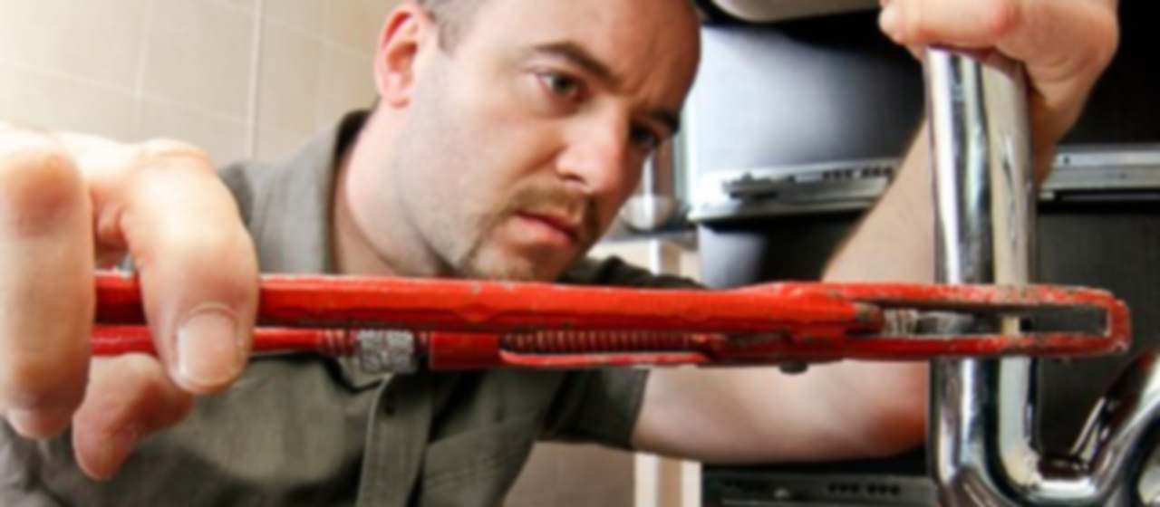Técnico con llave grifa desmontando el sifón de un fregadero de cocina atascado