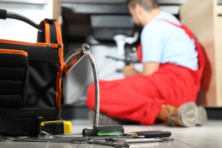 Técnico de desatascos con su equipo de herramientas Técnico de desatascos trabajando bajo un fregadero con la bolsa de herramientas en primer plano