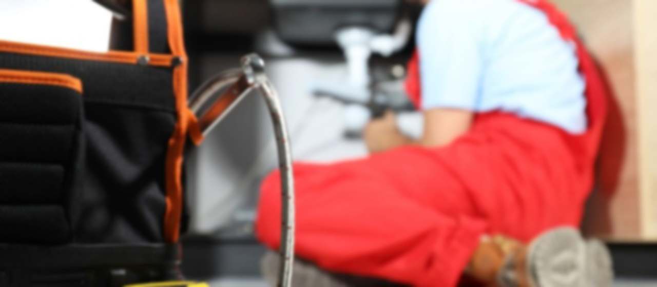 Técnico de desatascos trabajando bajo un fregadero con la bolsa de herramientas en primer plano