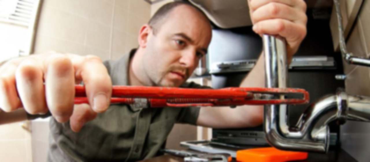 Técnico con llave grifa desmontando el sifón de un fregadero de cocina atascado